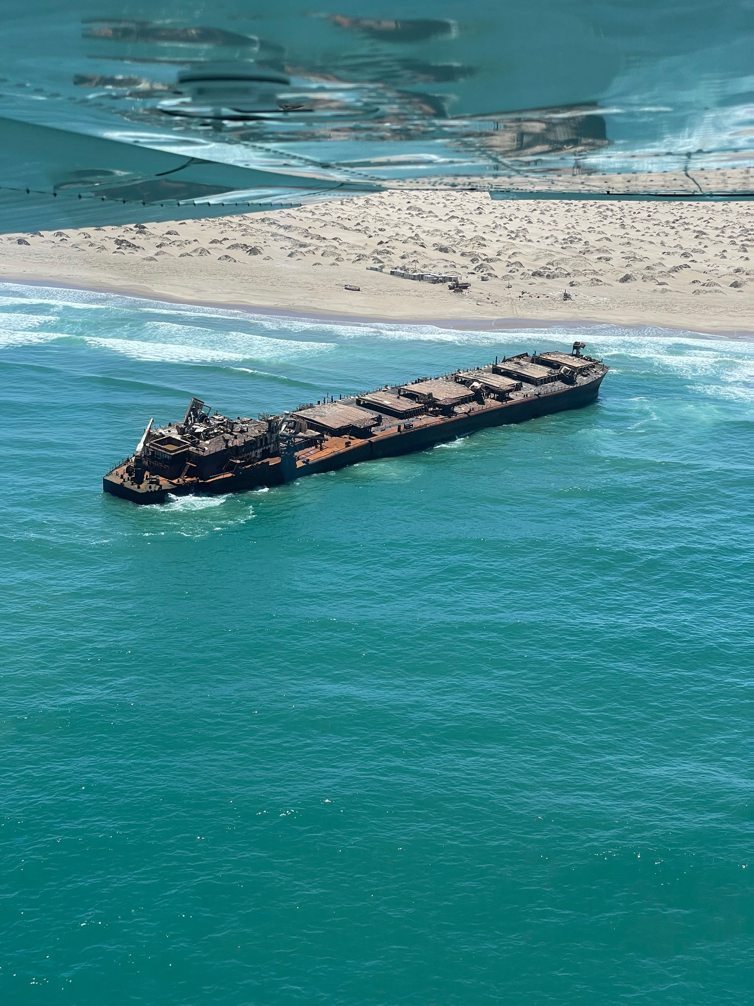 A shipwreck on a remote coastline seen from under the wing